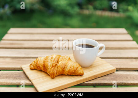White Coffee Cup And French Croissant On Wooden Table In Green Garden Stock Photo