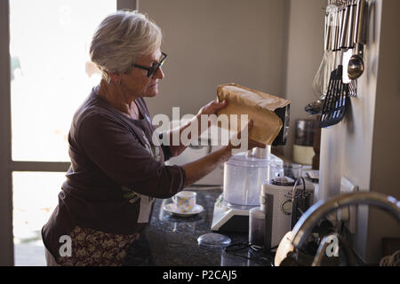 Senior woman putting milk in coffee maker Stock Photo