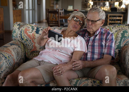 Senior couple taking selfie with mobile phone in living room Stock Photo