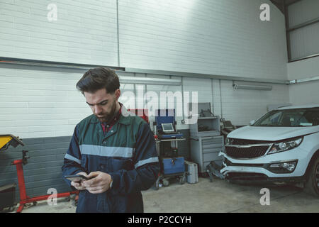 Mechanic using mobile phone while repairing car Stock Photo
