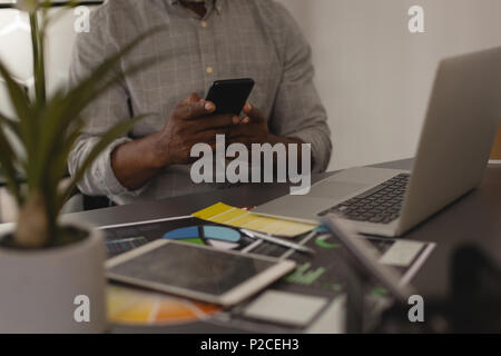 Senior graphic designer using mobile phone in office Stock Photo