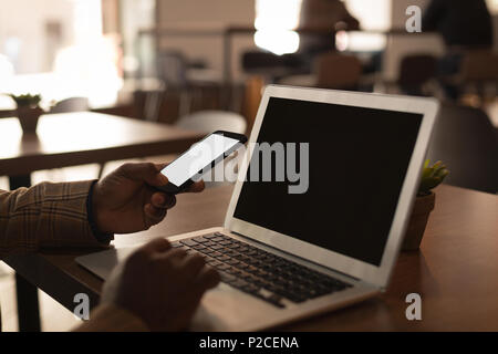 Senior graphic designer using laptop and mobile phone in cafeteria Stock Photo