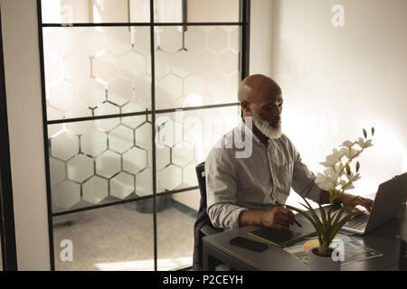 Senior graphic designer using graphics tablet and laptop at desk Stock Photo