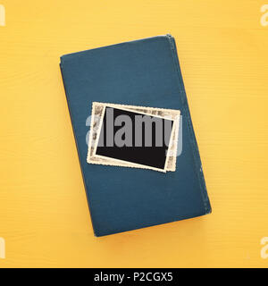 top view of blank photo frames over old book on yellow wooden background Stock Photo