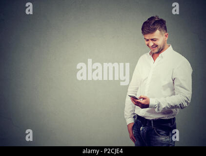Handsome stylish man holding and using smartphone and laughing on gray background Stock Photo