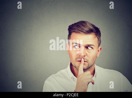 Man asking for silence and secrecy holding finger on lips and looking away in conspiracy Stock Photo