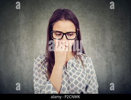 Nervous woman biting nails and looking down feeling insecure Stock Photo