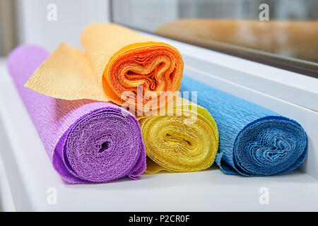 Four rolls of crumpled colored paper lie on windowsill. Stock Photo