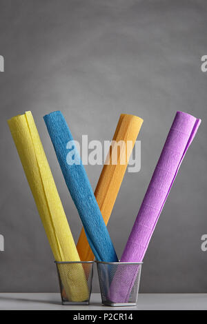 Few  multy-colored rolls of wrinkly creped paper, twisted into rolls and placed vertically in metal baskets on gray background. Stock Photo