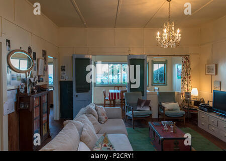 Living space at dusk of old bach / beach house. lights on. couch. Historic Pourerere Bach / Beach House, Hawke's Bay, New Zealand with new addition by Stock Photo