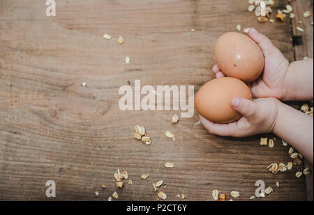 A child holding two brown, farm fresh eggs over a wooden table with oats around it. Stock Photo