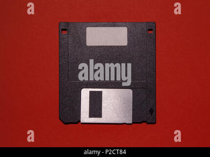 An obsolete floppy disk on a red background. You can write something on the blank label. Stock Photo
