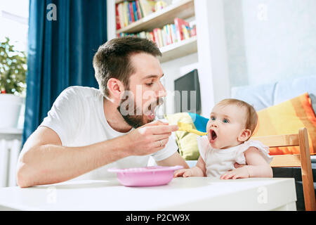Good looking young man eating breakfast and feeding her baby girl at home