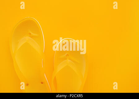 Top view of yellow flip flops pair on same color background with copy space. Beach sandals or slippers in minimalistic warm summer toned composition. Stock Photo