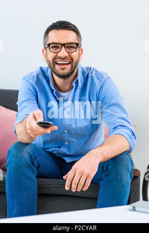 portrait of cheerful man changing channels while watching tv at home Stock Photo