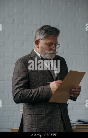 senior man in tweed suit writing letter in front of white brick wall Stock Photo