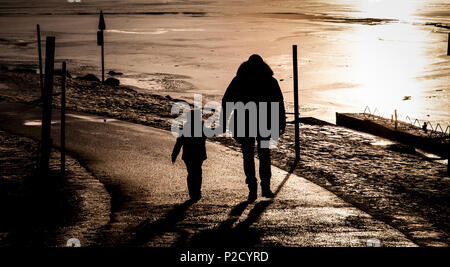 Silhouette of a father hand in hand with son near a frozen lake during sunset Stock Photo