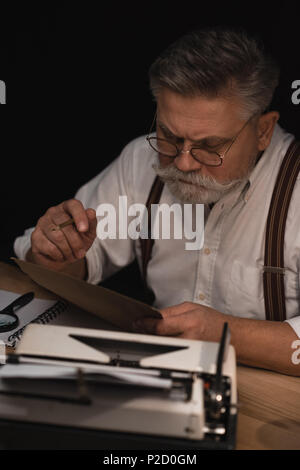 serious senior writer working with manuscript isolated on black Stock Photo