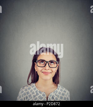 Young content woman in glasses looking up happily having idea and dreaming on gray background. Stock Photo