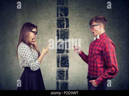 Shocked young couple man and woman separated by wall texting each other on mobile phone Stock Photo