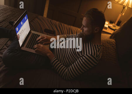Man sitting on bed in dark room using his laptop Stock Photo