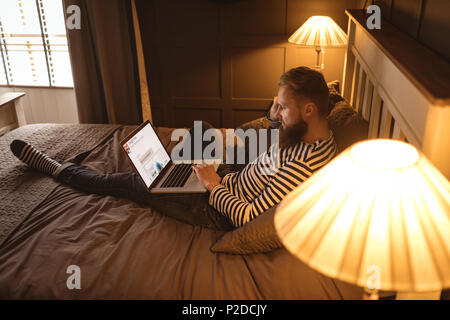 Man lying on bed while using laptop Stock Photo
