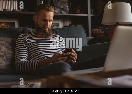 Man sitting on sofa using his mobile phone Stock Photo