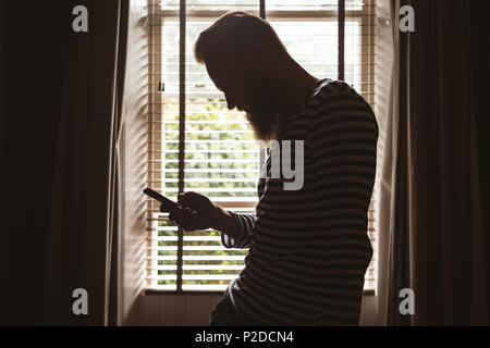 Man standing near window using his mobile phone Stock Photo