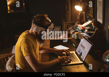 Man sitting on chair wearing virtual reality headset using his laptop Stock Photo