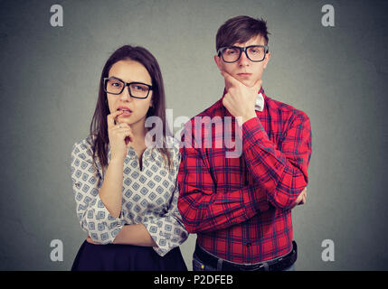 Young eccentric man and woman looking suspicious while standing on gray and looking at camera through glasses. Stock Photo