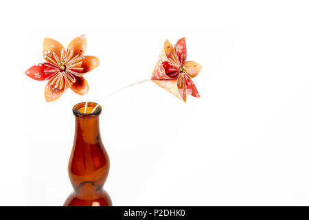 Close up of two orange origami flowers in dark glass bottle on white background. Stock Photo