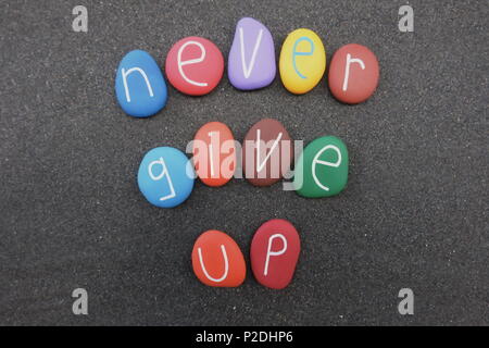 Never give up, motivational  phrase composed with colored stones over black volcanic sand Stock Photo