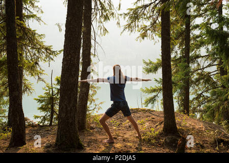 Fit man performing stretching exercise in a lush green forest Stock Photo