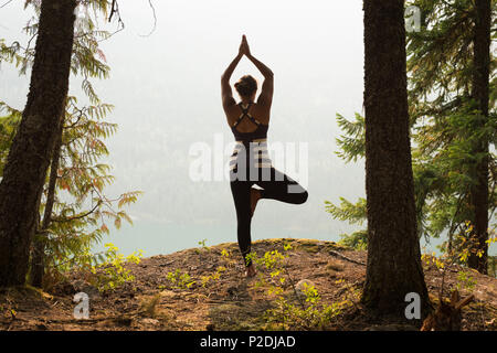 Fit woman performing stretching exercise in a lush green forest Stock Photo