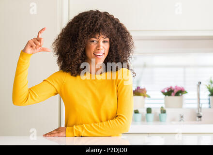 African american woman wearing yellow sweater at kitchen smiling and confident gesturing with hand doing size sign with fingers while looking and the  Stock Photo