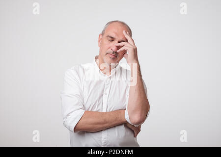 Close up portrait of handsome mature man in white shirt holding hand near face and thinking about work or life problem. Stock Photo
