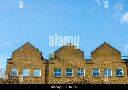 Converted red brick industrial building against a blue sky in London Stock Photo