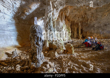 A young woman and a young man with trekking gear sitting and studying a map in a huge cave with dripstones above the sea, in mou Stock Photo