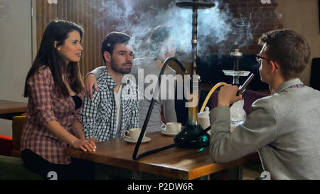 Young friends smoking hookah in shisha cafe Stock Photo