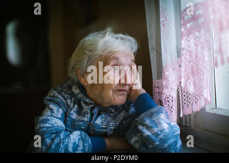 An elderly pensioner woman looks out the window sadly. Stock Photo