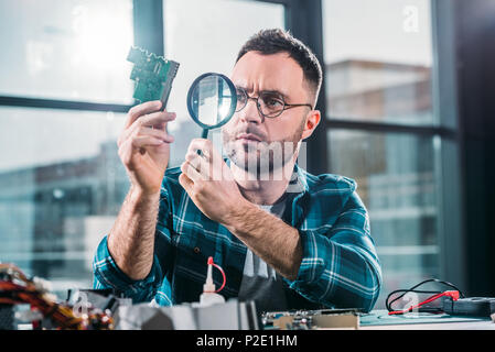Hardware engineer looking at circuit board through magnifying glass Stock Photo