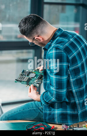 Rear view of engineer looking at circuit board Stock Photo