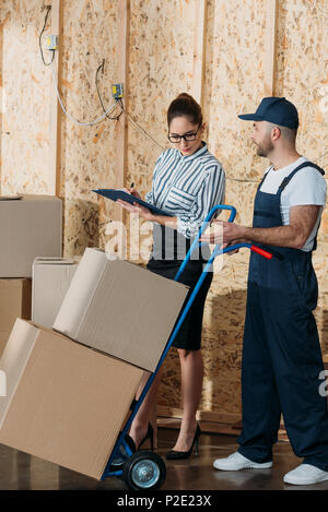 Businesswoman filling checklist while loader man carrying delivery cart Stock Photo