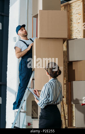 Businesswoman filling checklist while loader man standing on a ladder Stock Photo