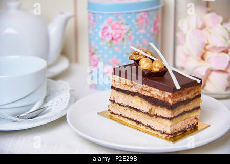 Chocolate cake with nuts on a plate near a cup, teapot and jar of marshmallows. Stock Photo