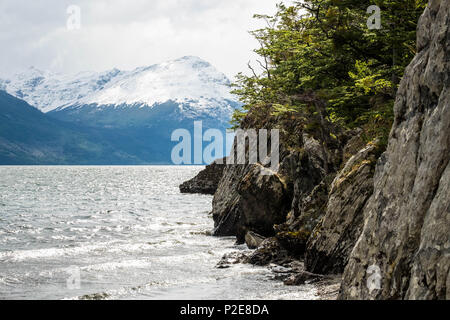 A cliff borders Lake Acigami in the national park of Tierra del Fuego, mountains are on the other side. This lake connects Argentina and Chile. Stock Photo
