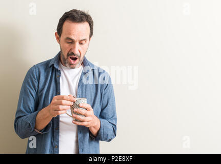 Senior man drinking coffee in a mug scared in shock with a surprise face, afraid and excited with fear expression Stock Photo
