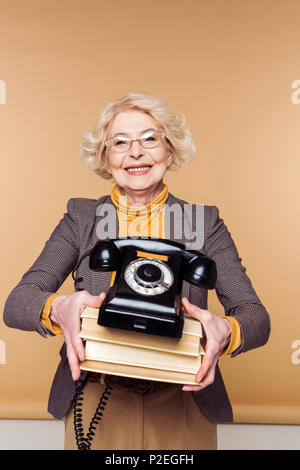 stylish senior woman in eyeglasses holding rotary phone and stack of books Stock Photo