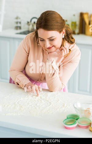beautiful woman painting heart with flour on kitchen counter Stock Photo