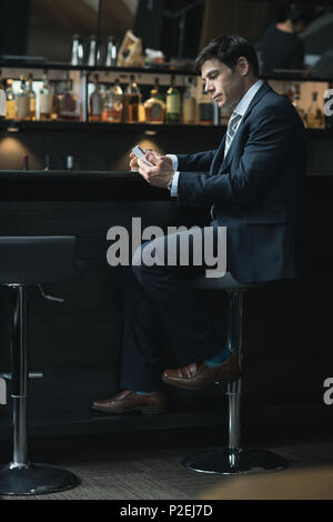 Businessman using mobile phone while having whiskey Stock Photo